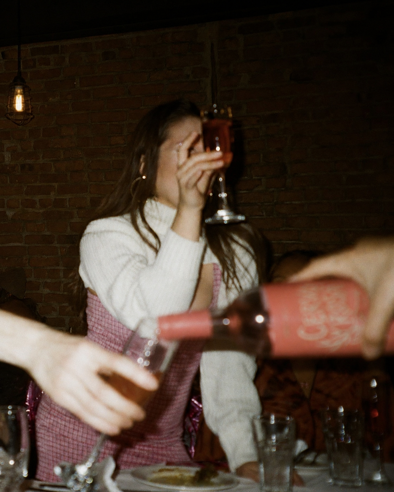 A woman at a low-lit party, flash gun style image, holding a glass of Sila wine. 